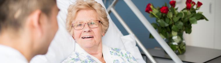 afbeelding van een oudere mevrouw in een ziekenhuis bed die met een arts praat