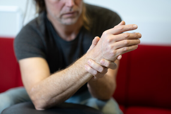 Foto van een patiënt die zijn hand om zijn pols legt omdat hij pijn heeft