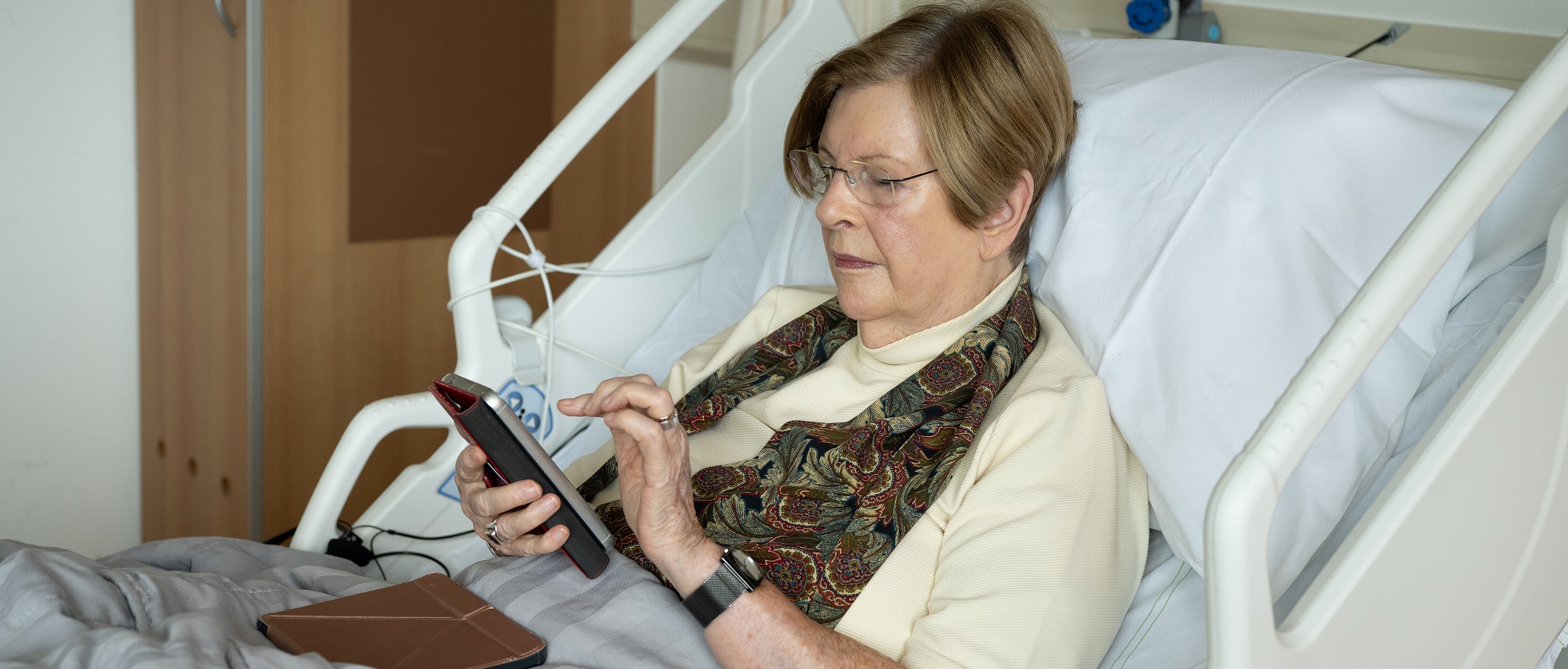 Foto van een patiënt die in een ziekenhuisbed op haar telefoon zit