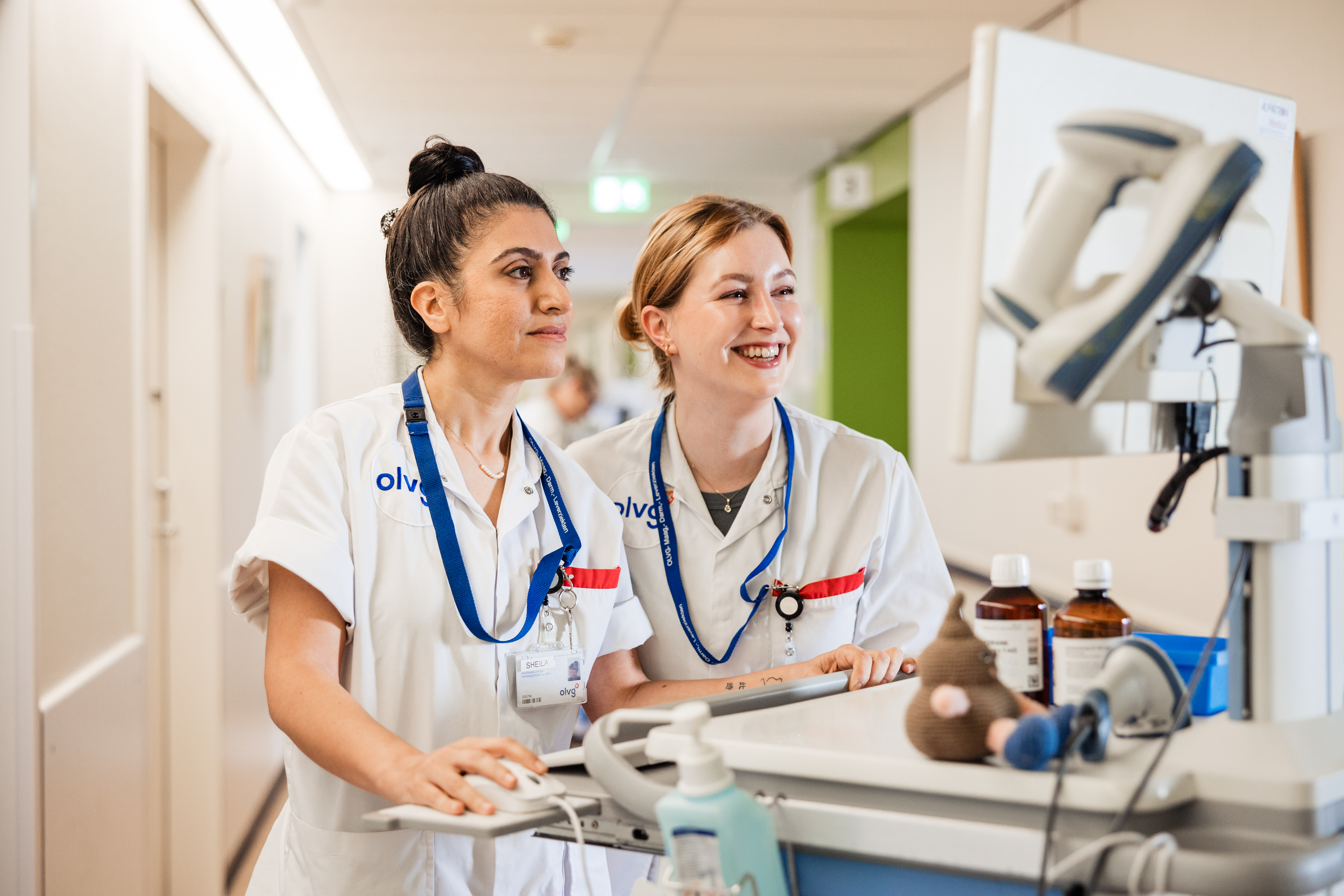 Twee vrouwelijke OLVG-verpleegkundigen kijken samen op een COW (Computer on Wheels) naar patiëntgegevens.