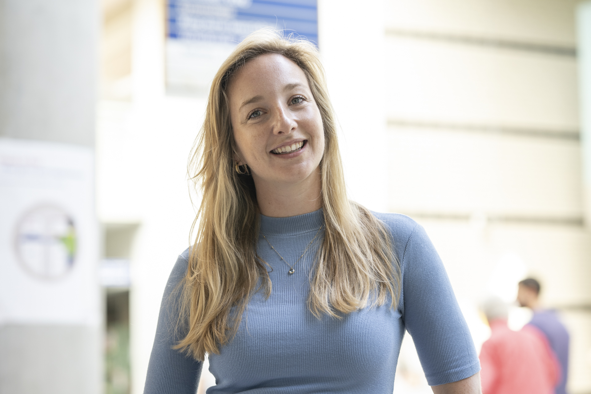 Een lachende, blonde vrouw met een blauw truitje met haar hoofd licht naar rechts gekanteld